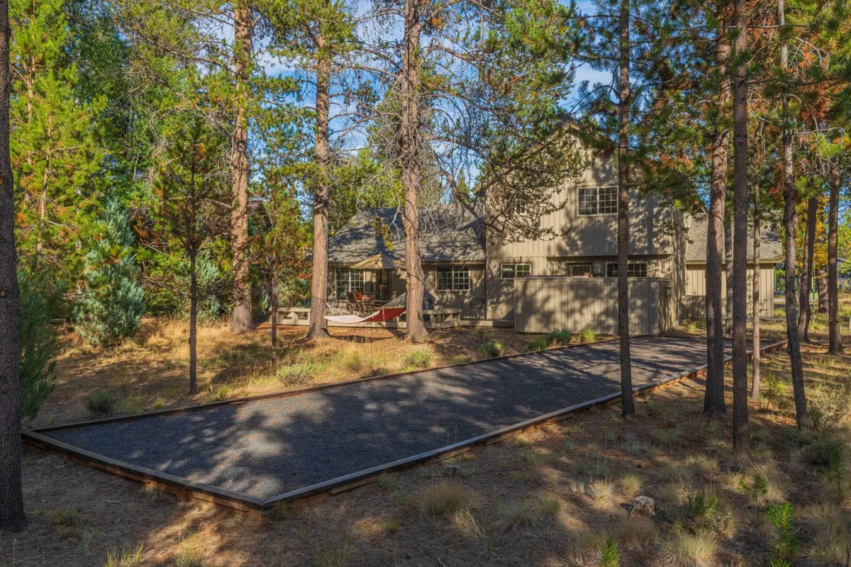 A peaceful view of the house’s exterior, featuring a welcoming pathway, a cozy seating area, and a backdrop of tall trees. The seating looks perfect for sunset views or stargazing, with ample space for guests to gather or unwind by themselves.