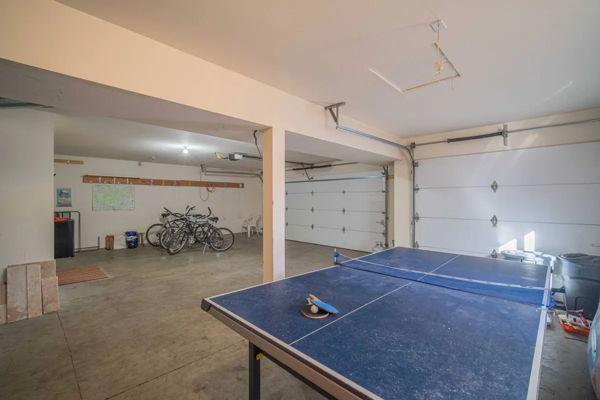 A vibrant garage game zone featuring a ping pong table and bicycles, with garage doors and ample natural light. The space feels casual and active, inviting friendly competition and leisure time with friends or family.