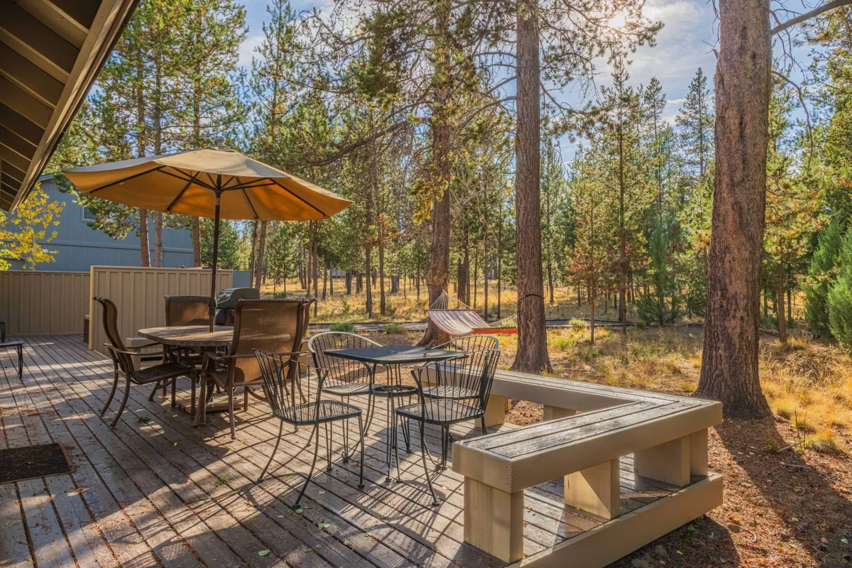 An inviting deck setup that includes a dining table with an umbrella and a hammock, all surrounded by mature trees. The area feels ready for outdoor meals, lazy afternoons, and unwinding after adventures, with a peaceful, resort-style atmosphere.
