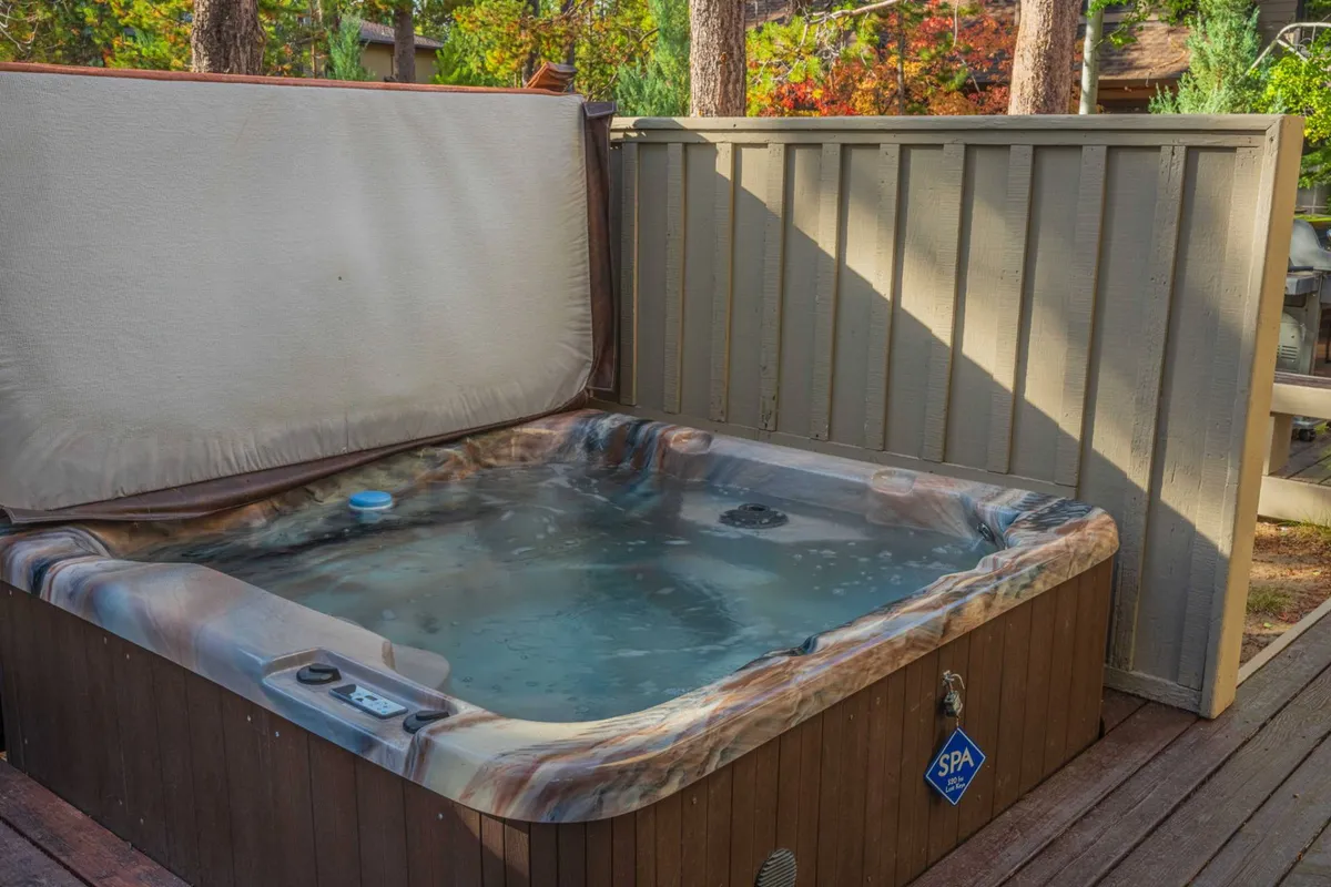 A tranquil outdoor deck area featuring a secluded hot tub surrounded by tall trees, with spacious decking and subtle evening light that hints at stargazing opportunities. The space feels private and inviting, providing both a connection to nature and a sense of relaxation.