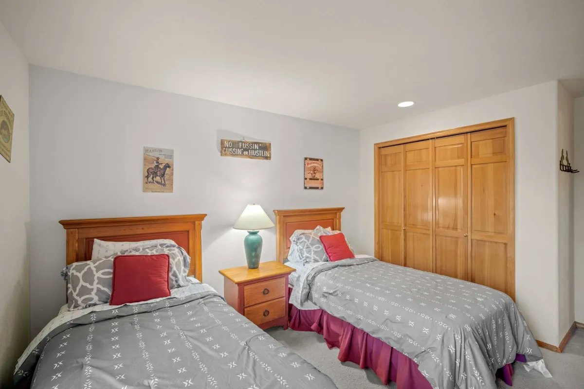 A cozy twin bedroom with two twin beds neatly made, a central nightstand with lamp, and decorative wall art. The ambiance is relaxed and welcoming, ideal for younger guests or friends sharing the space.