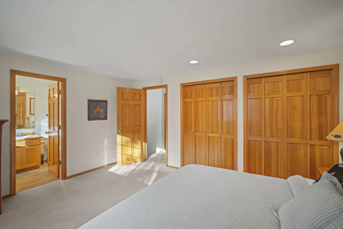 A spacious bedroom featuring a king bed, wooden closet doors, and multiple doorways. The room is bathed in soft natural light, with calm tones and gentle decor, creating a sense of peaceful solitude and comfort ideal for relaxing after a busy day.