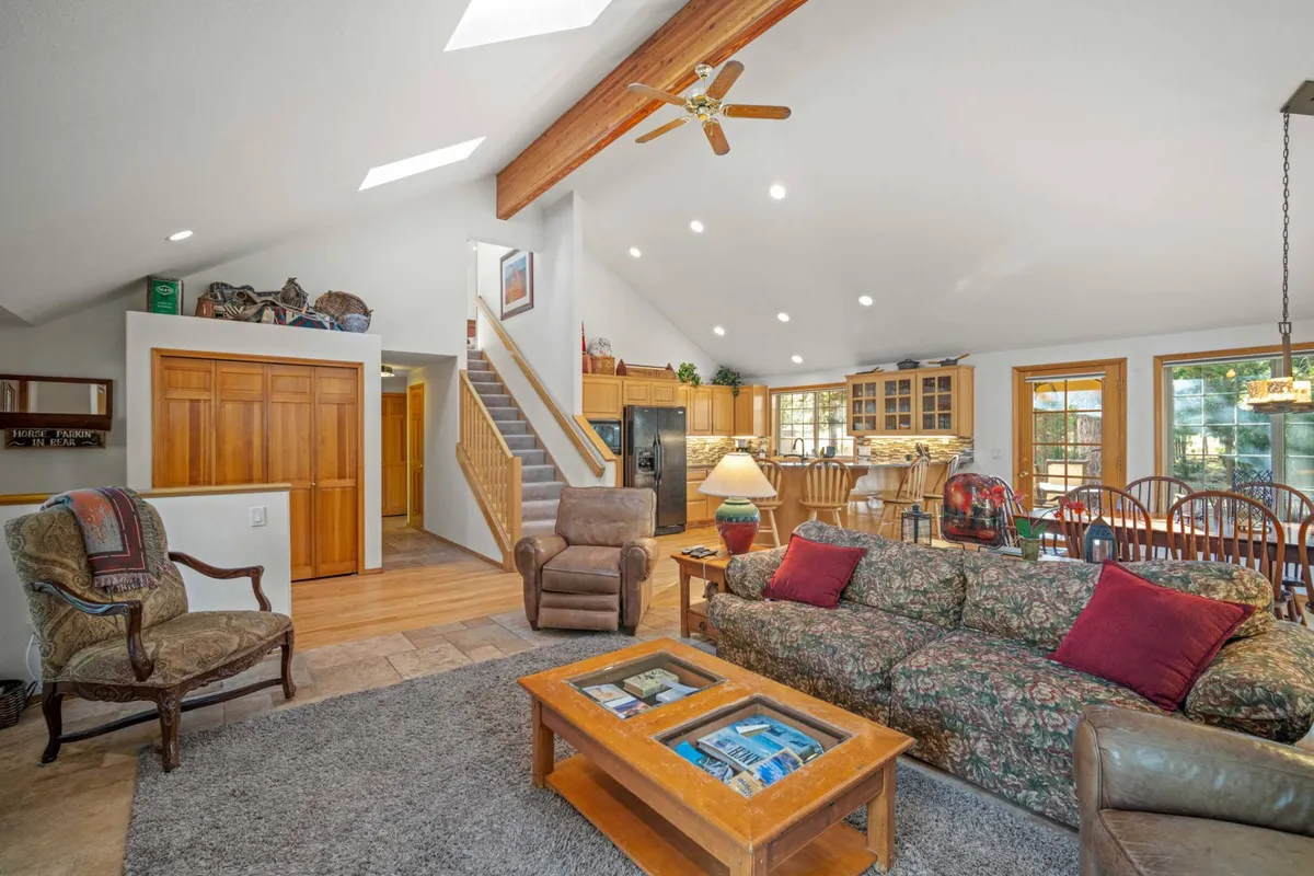 A spacious living area with a plush sofa adorned with decorative cushions, a coffee table, and a wooden dining area visible in the background. The layout flows seamlessly from the living to the dining space, with stairway access to the upper level visible, capturing a sense of openness and family-friendly design.