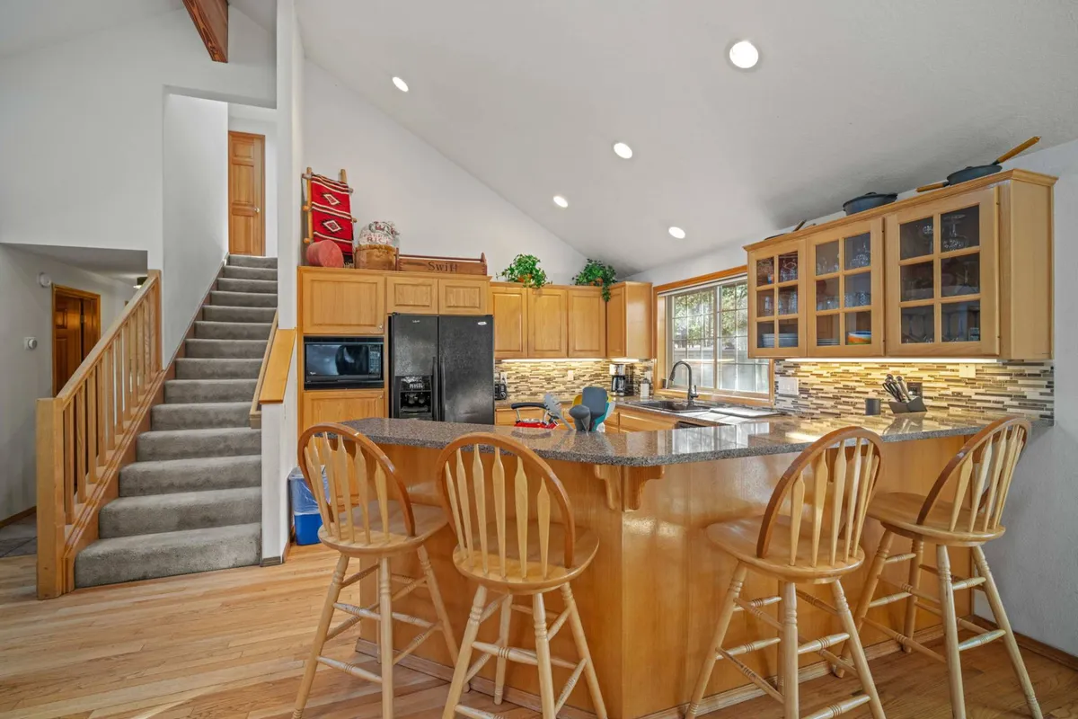 A modern kitchen featuring a spacious island with granite countertops, sleek stainless steel appliances, bar stools lined up for casual seating, and a large window letting in natural light. The layout is open and inviting, perfect for both cooking and entertaining.