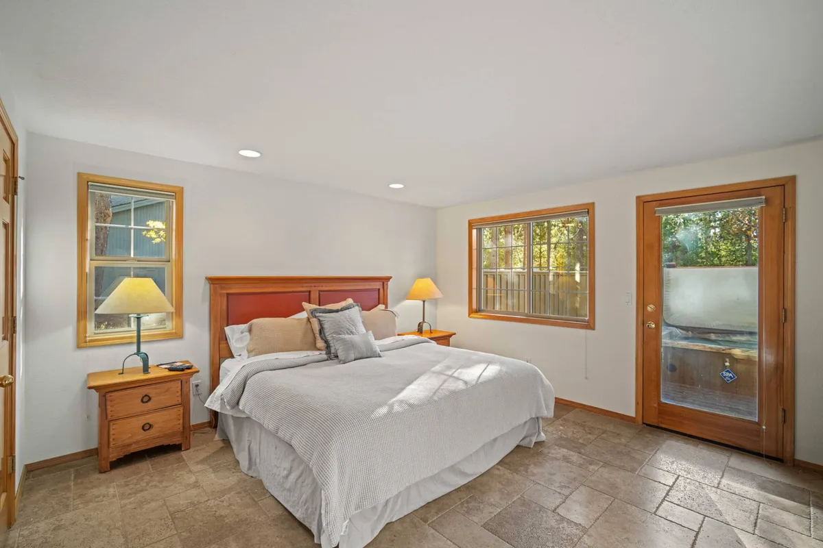 A tranquil queen bedroom with a cozy bed, bedside lamp, windows letting in gentle light, and a door. The setup is inviting, providing both comfort and privacy for guests.